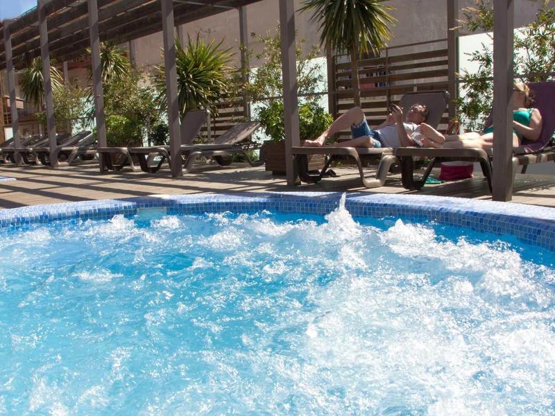 Sprudelnder Whirlpool im Außenbereich mit Holzdach und Sonne am klaren Himmel.