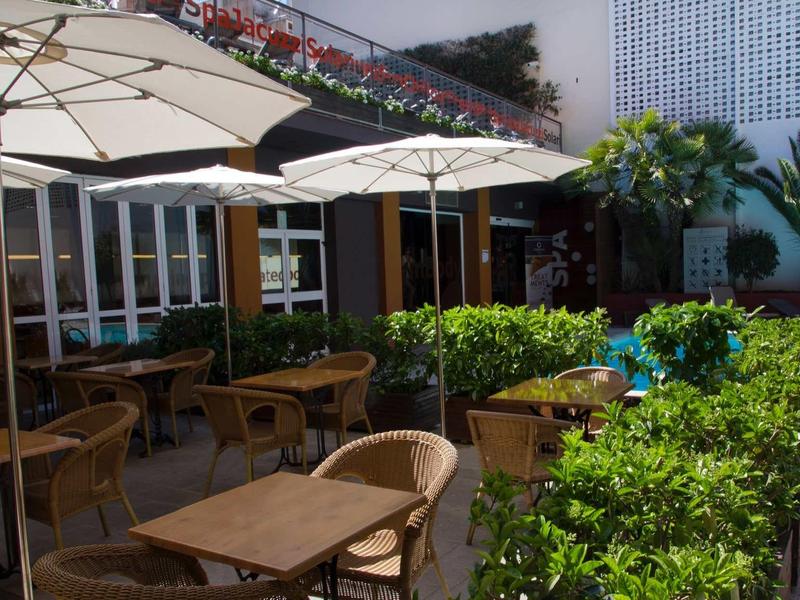 Außerhalb sitzender Bereich mit Holztischen, Rattanstühlen, Sonnenschirmen und grünen Pflanzen.