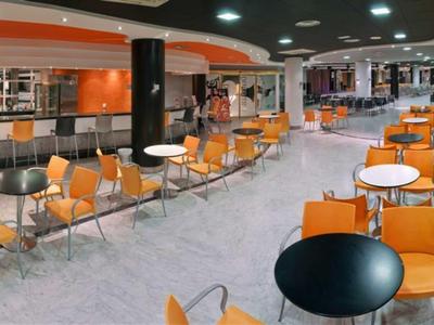 Interiér moderní, světlé kavárny s oranžovými židlemi a černými stoly.