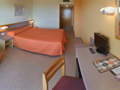 Hotelový pokoj se dvěma lůžky, psacím stolem, televizí a neutrálními zdmi.