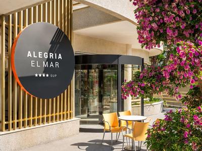 Hotel entrance with round sign and seating area with table and chairs next to blooming tree.