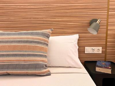 Bed with white pillow and striped pillow, night lamp, and book on bedside table.