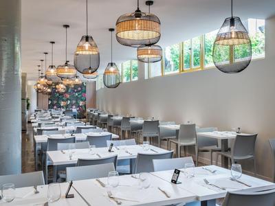 Modern restaurant with white tables, gray chairs, and hanging ceiling lamps.