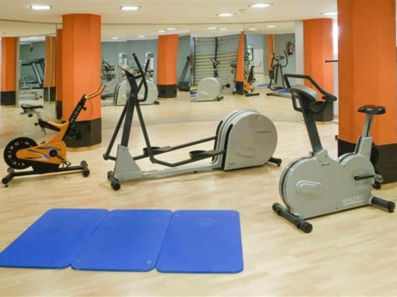 Dobře osvětlená tělocvična s posilovacími stroji a modrými podložkami na zemi