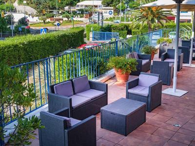 Moderní terasa s pevnými lounge nábytkem s výhledem na zahradu a kopce za slunečného počasí.