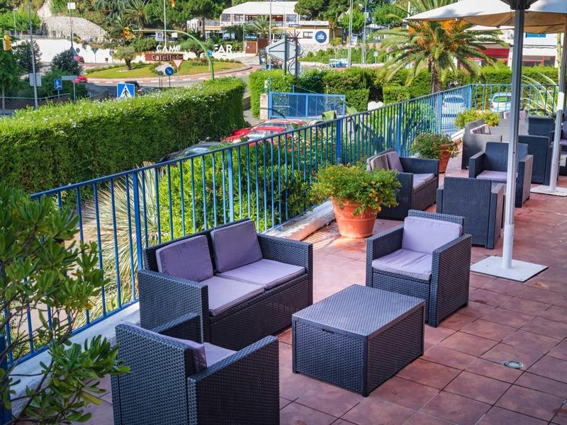 Moderní terasa s pevnými lounge nábytkem s výhledem na zahradu a kopce za slunečného počasí.