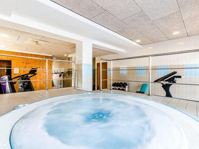 Moderner Fitnessraum mit Whirlpool, Spiegelwand und Laufband in hellem, minimalistischem Design.