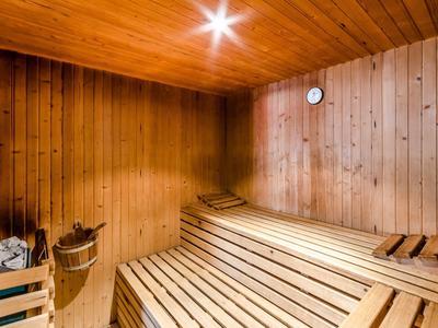Sauna mit hellen Holzlattenbänken, Holzwänden, Eimer, Schöpflöffel und runder Uhr an der Wand.