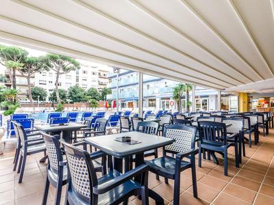 Freiluftrestaurant mit blauen Tischen, Stühlen und Überdachung neben einem Pool in hellem Umfeld.