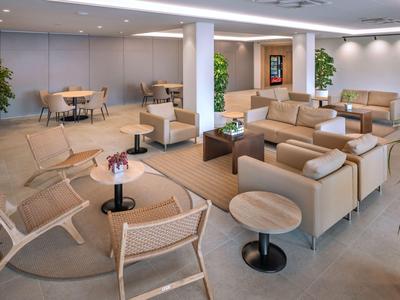 Modern eingerichteter Aufenthaltsraum mit Sesseln, Tischen und Pflanzen in einem Hotel.