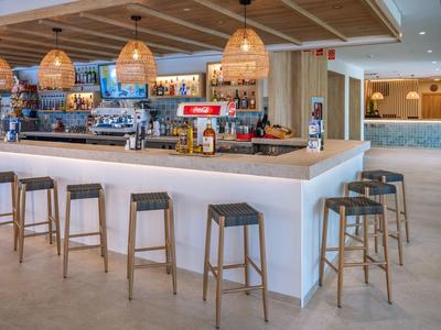 Moderner Barbereich mit weißen Wänden, Holzstühlen und warmen Hängelampen in hellem Raum.