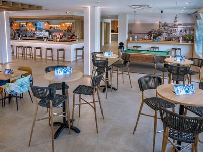 Heller, moderner Gastraum mit runden Tischen, schwarzen Stühlen und langer Bar im Hintergrund.