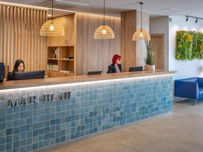 Moderner Empfangsbereich mit blauen Kacheln, Holzvertäfelung, Hängeleuchten und grüner Wanddekoration.