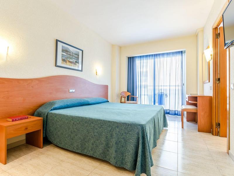 Ein schlicht eingerichtetes Hotelzimmer mit Doppelbett, Nachttisch, Schreibtisch und Balkon.