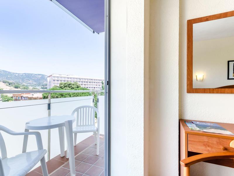Balkon mit weißem Tisch und Stühlen, daneben Spiegel und Schreibtisch in hellem Zimmer.