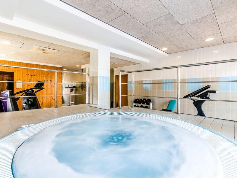 Moderner Fitnessraum mit Whirlpool, Spiegelwand und Laufband in hellem, minimalistischem Design.