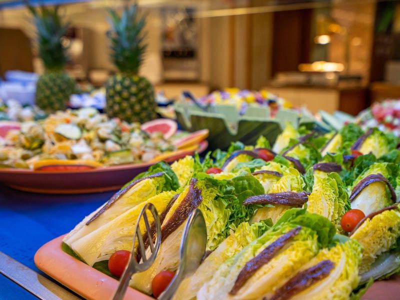 Bunter Buffet-Tisch mit frischen Salaten, Ananas und verschiedenen Zutaten auf blauen Tüchern.