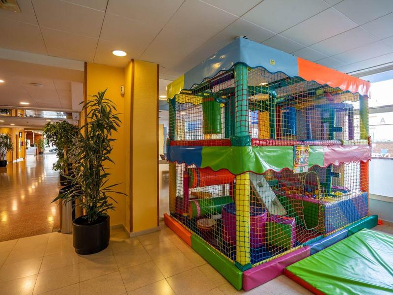 Bunter Indoor-Kletterspielplatz mit weichen Matten in einem hellen Raum neben Pflanzen.