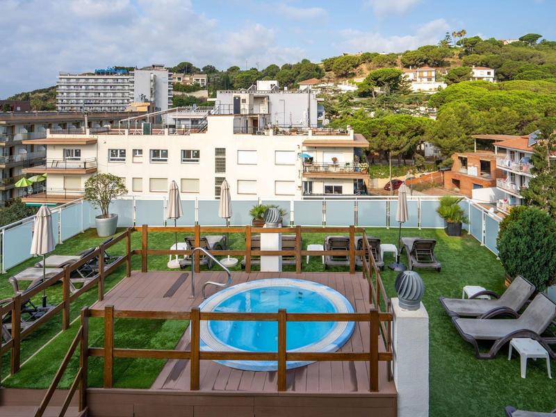Balkon mit Holzgeländer, kleinem Pool, zwei Liegestühlen und umliegenden Gebäuden im Hintergrund.