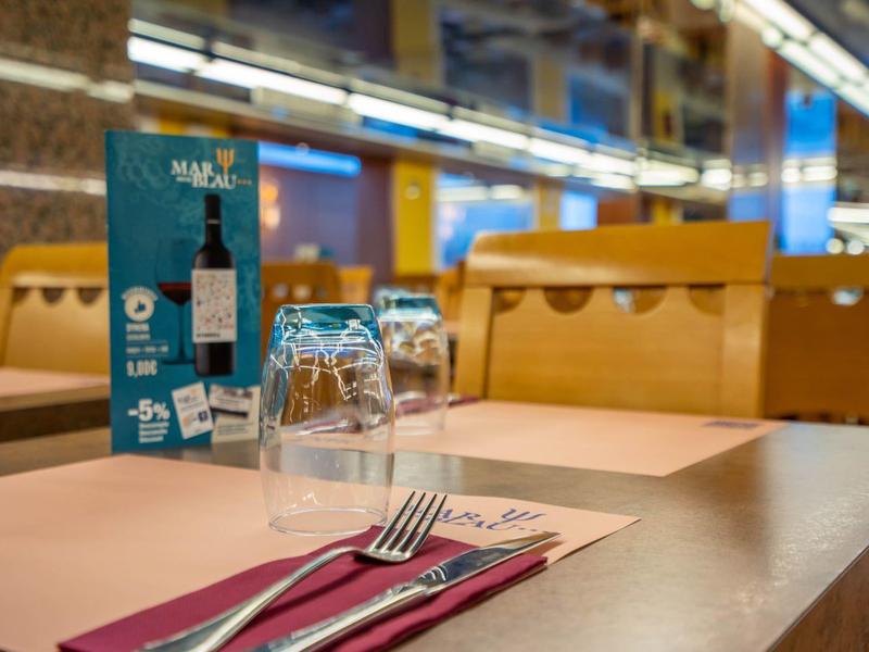 Restaurant-Tisch mit Besteck, Gläsern und Menü, Holzstühle und warme Beleuchtung im Hintergrund.