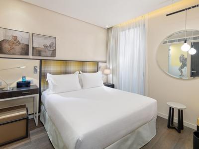 Modern hotel room with double bed, desk, and round mirror on the wall.