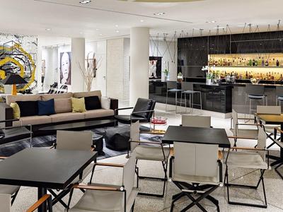 Modern hotel lobby with seating areas, tables, and a lit bar area in the background.