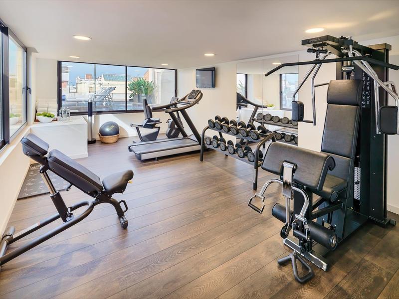 Bright gym with large windows, wooden floor, weight machines, dumbbells, and exercise equipment.