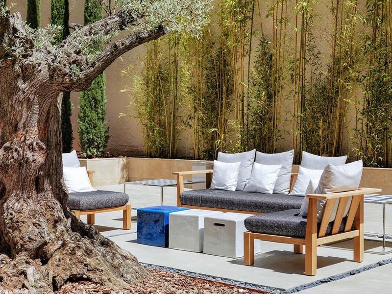 Modern seating area with wooden furniture and cushions next to a large tree in the garden.