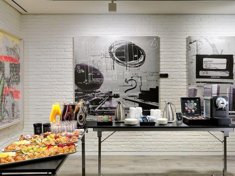 Buffet with pastries and drinks in front of a white brick wall with modern art.