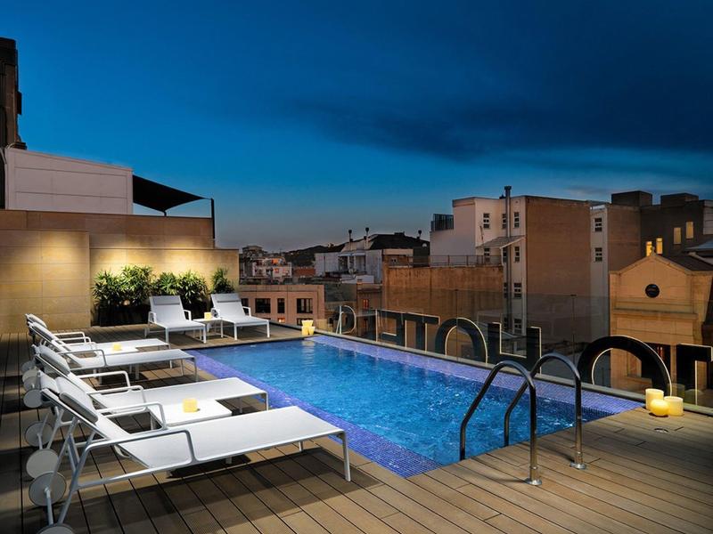 Rooftop terrace with illuminated pool and loungers at night overlooking the city.