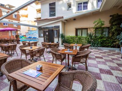 Dziedziniec hotelowy z drewnianymi stołami i krzesłami, otoczony roślinami i budynkami.