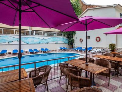 Basen hotelowy z niebieskimi leżakami i stołami z krzesłami pod różowymi parasolami.