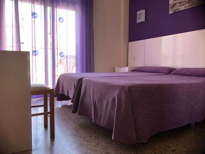 Pokój hotelowy z dwoma łóżkami i fioletowymi narzutami obok okna z zasłonami.