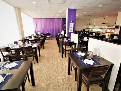 Jasna restauracja z ciemnymi drewnianymi meblami, nakrytymi stołami i fioletową zasłoną w tle.