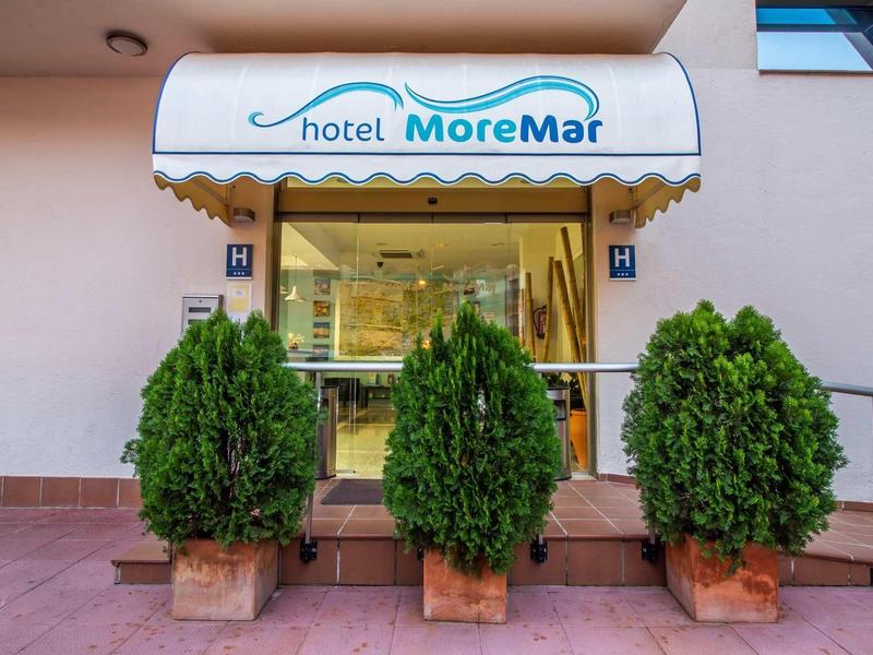 Wejście do Hotelu MoreMar z trzema dużymi zielonymi roślinami w doniczkach na przodzie.