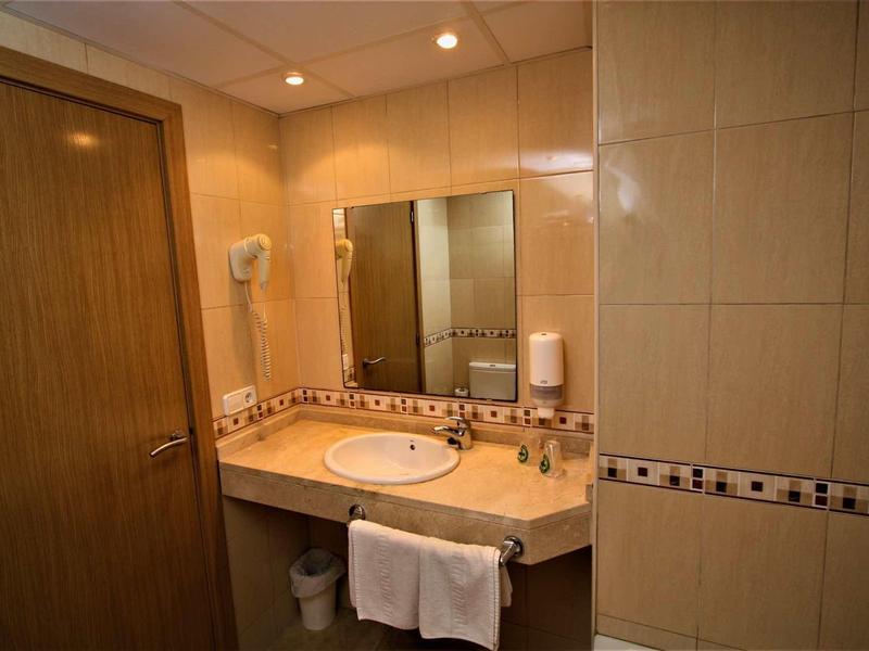 Jasno oświetlona łazienka z umywalką, dużym lustrem i ręcznikiem pod blatem.