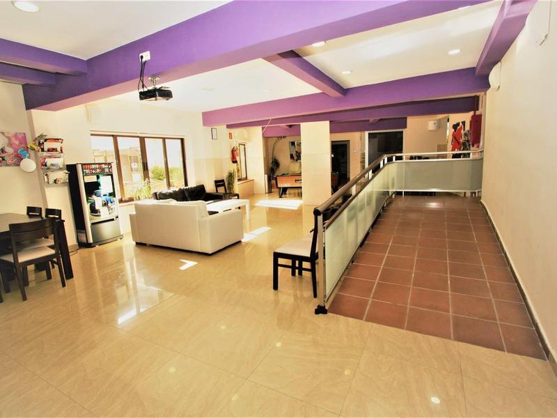 Przestronny, jasny salon hotelowy z fioletowymi belkami sufitowymi i wygodnymi miejscami do siedzenia.