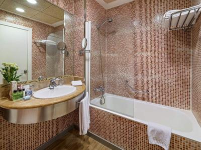 Salle de bain moderne avec carrelage en mosaïque, baignoire, lavabo et miroir dans un hôtel.