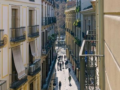Schmale Straße mit historischen Gebäuden und Menschen, die in Richtung moderner Hochhausfassade gehen.
