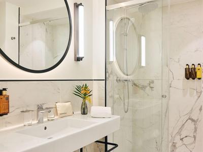 Modernes Badezimmer mit weißem Waschbecken, rundem Spiegel und Duschkabine mit Marmorwand.