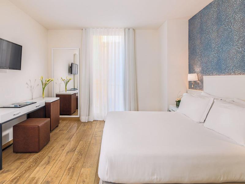 Chambre d'hôtel lumineuse avec grand lit, TV, bureau et sol en bois.