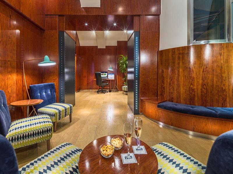 Salon d'hôtel confortable avec murs en bois, fauteuils à motifs et petite table ronde avec verres.