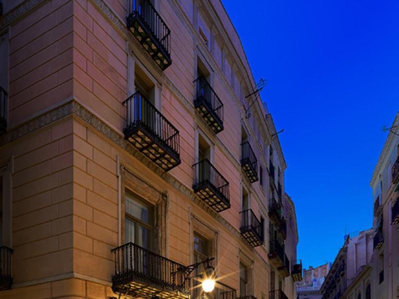 Rue étroite avec entrée d'hôtel éclairée chaleureusement sous un ciel bleu du soir.