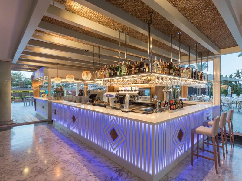 Bar moderno dell'hotel con luci blu e bicchieri sospesi in uno spazio aperto.