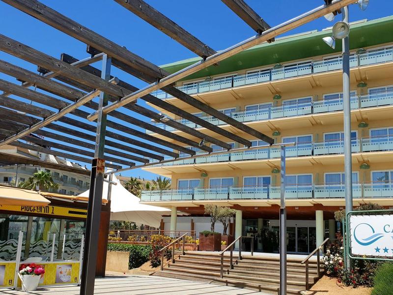 Ingresso moderno di un hotel con area esterna e pergolato sotto un cielo azzurro.