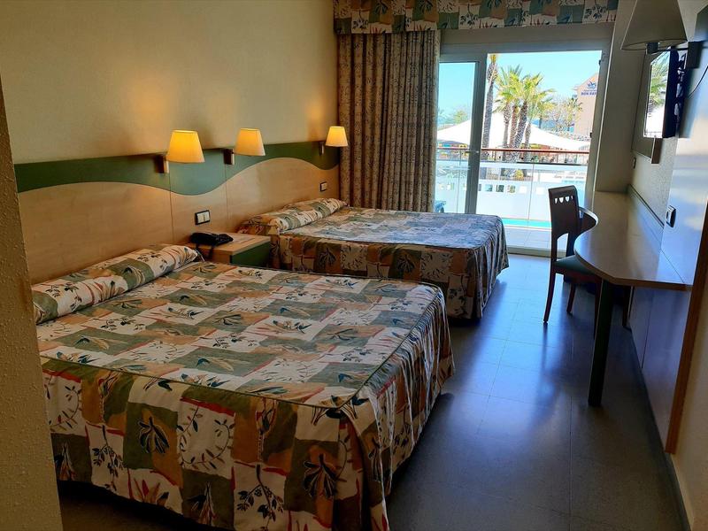 Camera d'hotel con due letti, vista sul balcone con piscina e palme, mobili in legno semplici.