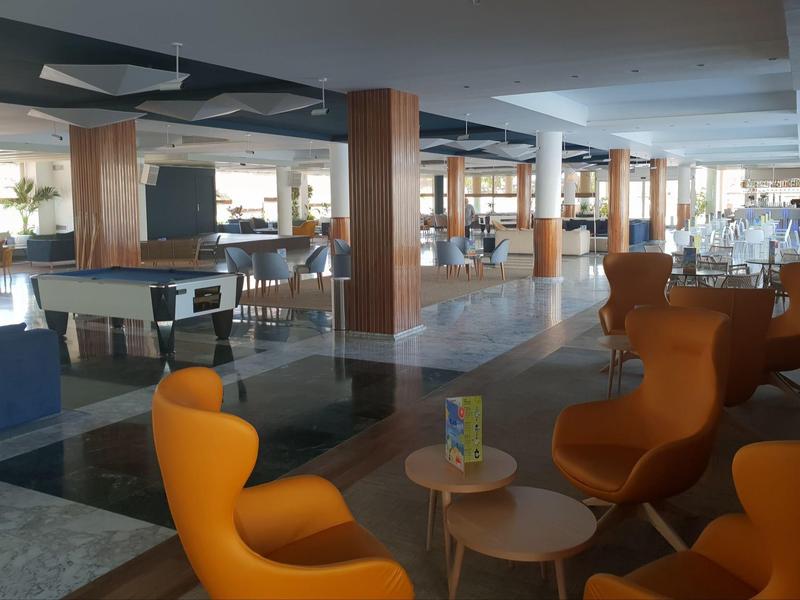 Lounge moderno dell'hotel con poltrone arancioni, tavoli e un tavolo da biliardo sullo sfondo.