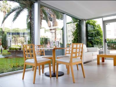 Espace moderne avec tables et chaises en bois à côté de grandes baies vitrées donnant sur un jardin.