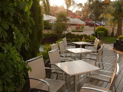 Terrazza con tavoli e sedie bianchi, circondata da piante e palme al tramonto.