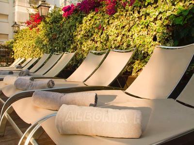 Chaises longues avec serviettes à côté de fleurs et d'un bâtiment au soleil.